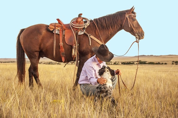 Lucky Lou agachado brincando com um cachorro aos pés de seu cavalo. Esta é sua história